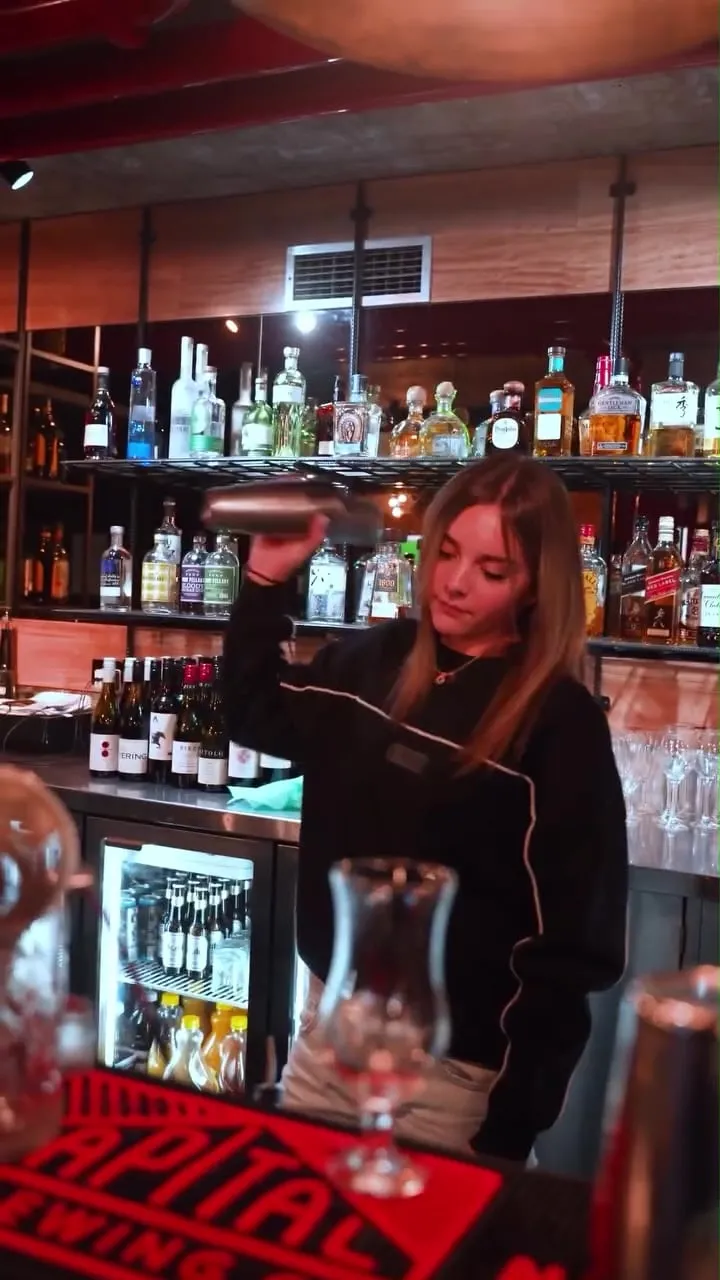 A bartender shaking a cocktail in front of the back bar