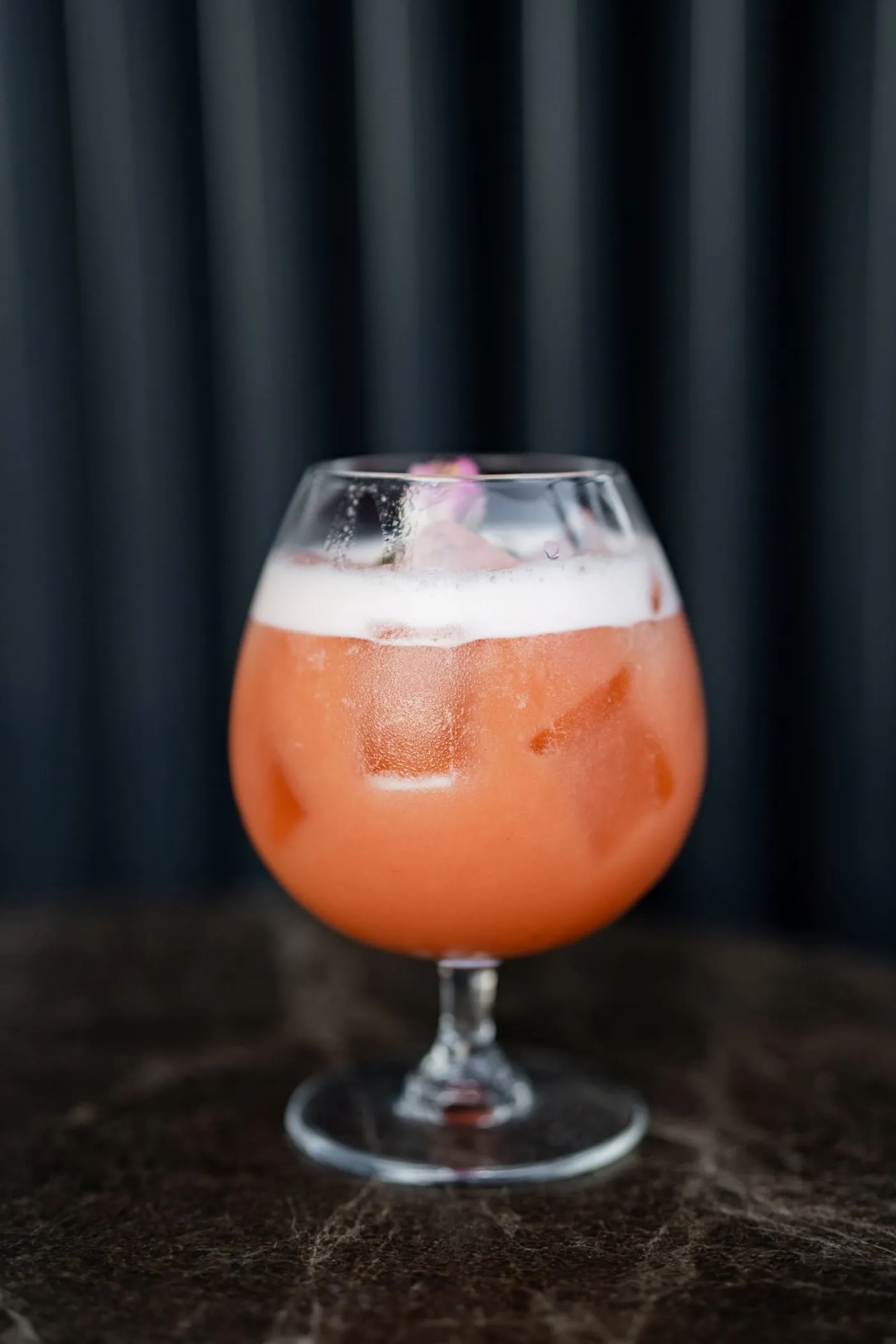 A peach-pink cocktail in a stemmed glass on a dark bar