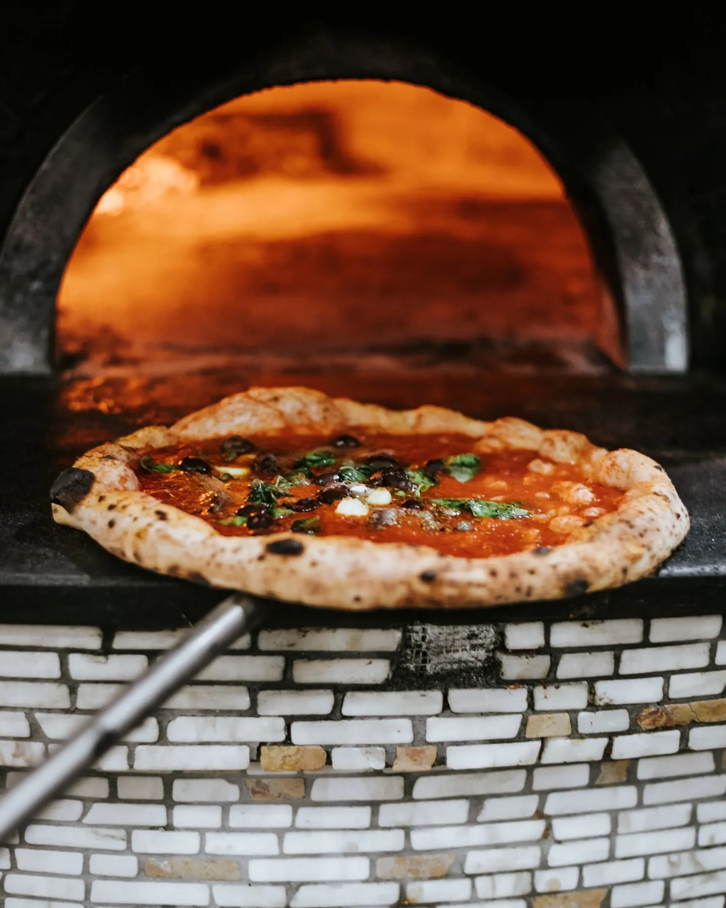 A pizza coming out of a brick oven on a peel