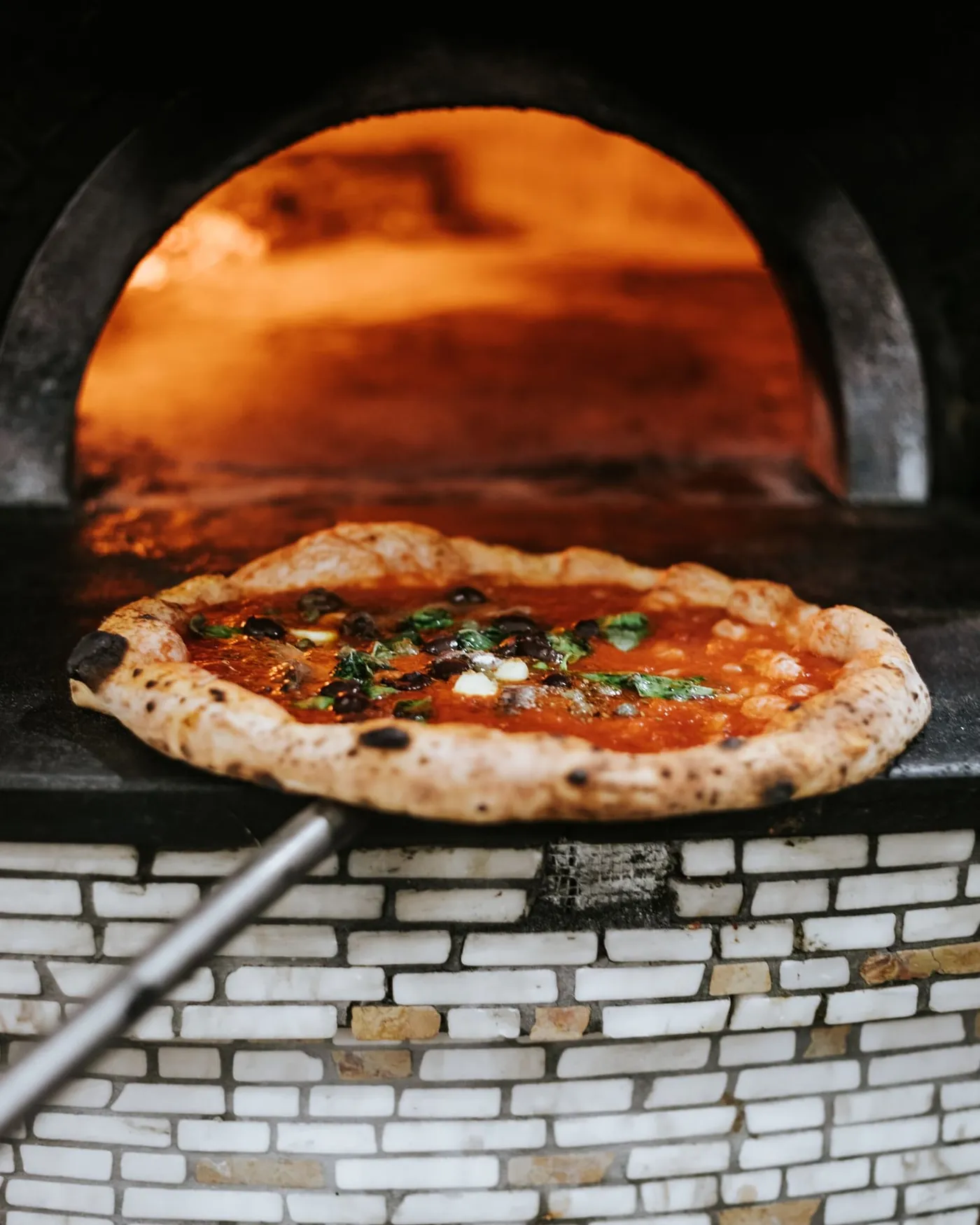 A pizza coming out of a brick oven on a peel