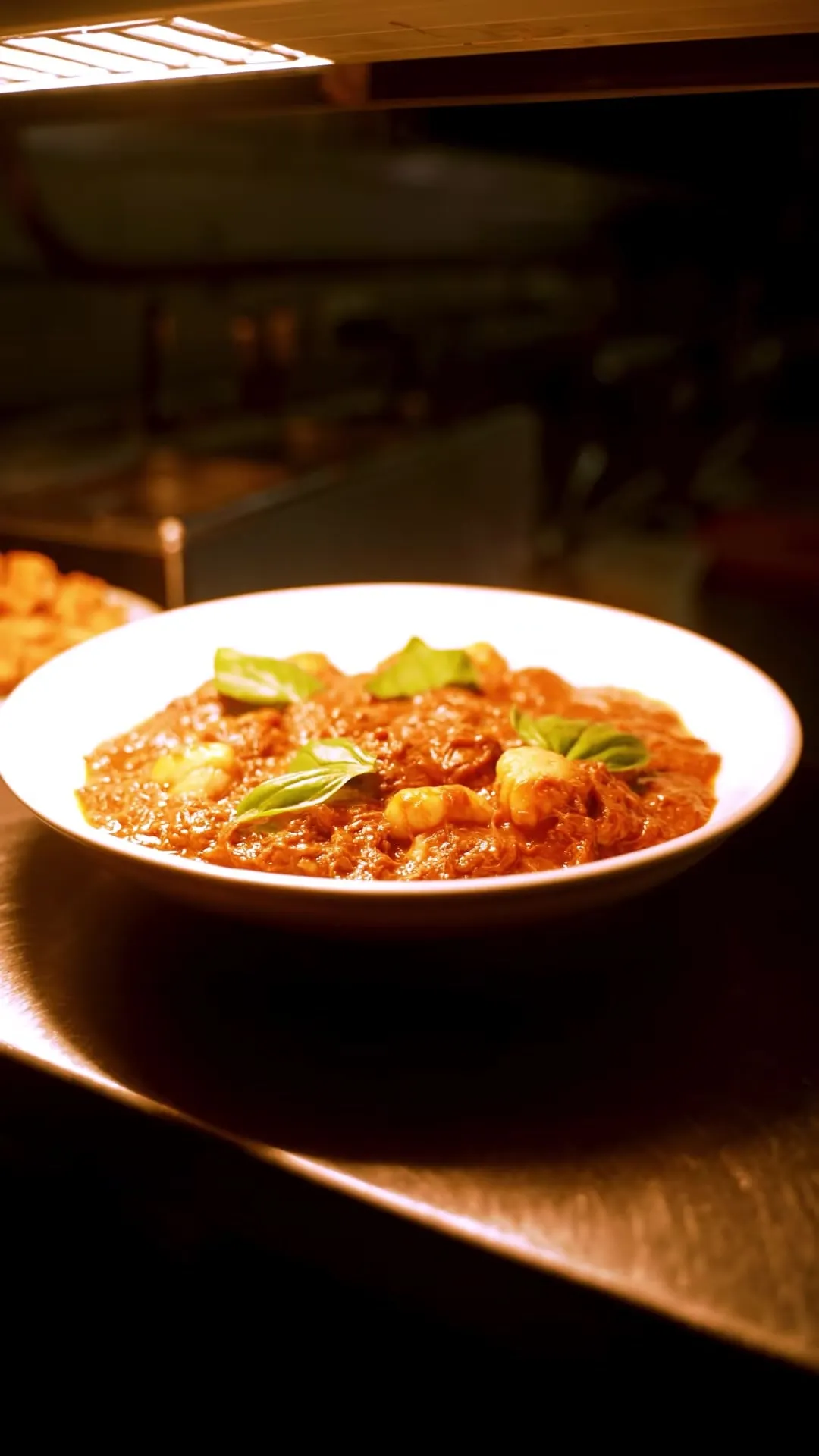 Braised lamb gnocchi with basil on the steel pass under the heat lamp