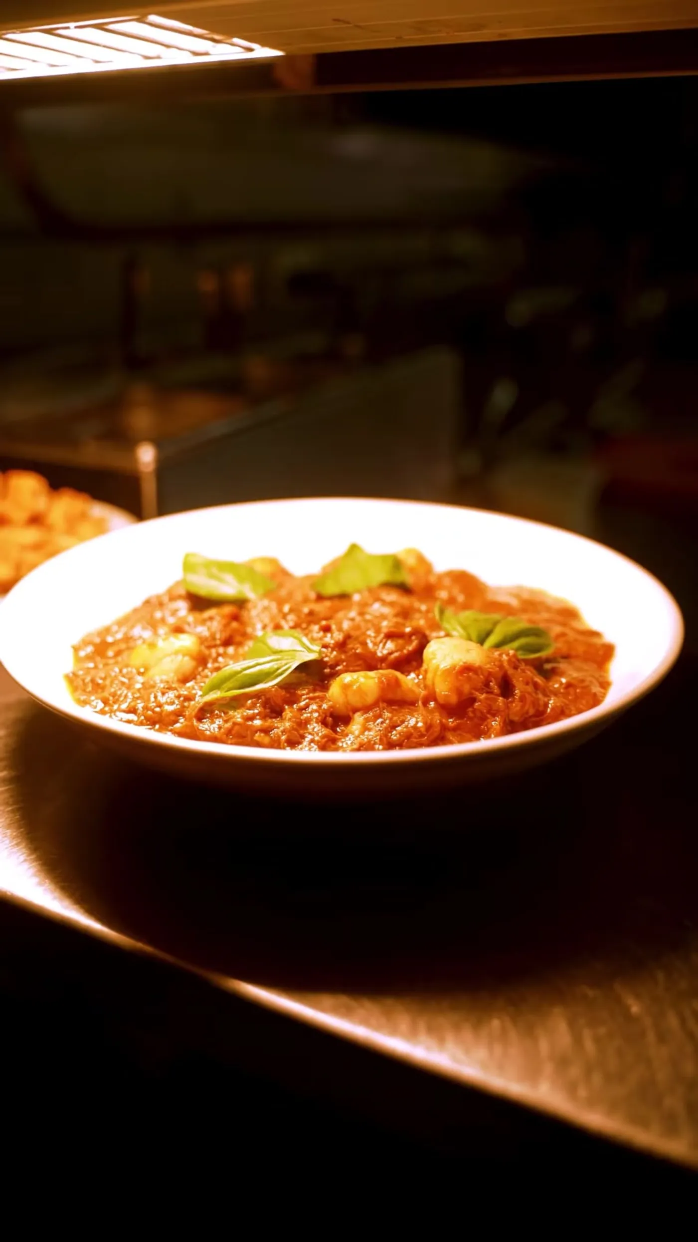 Braised lamb gnocchi with basil on the steel pass under the heat lamp