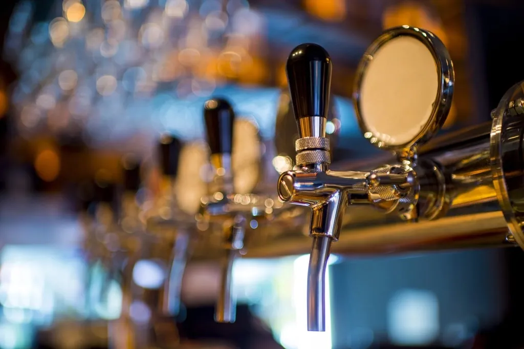 A row of brass beer taps along a bar in warm light